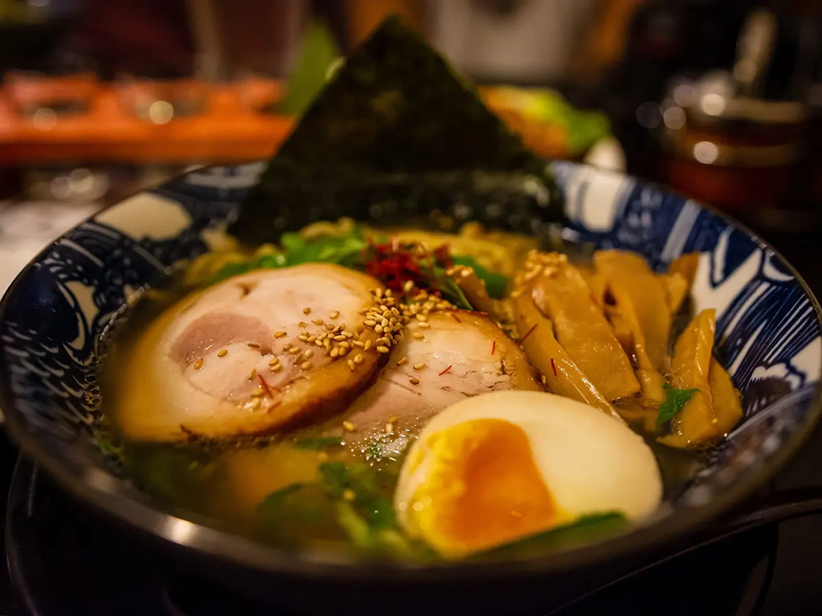 Tonkotsu Chashu Ramen presents a bowl of ramen in rich pork bone broth, topped with slices of tender chashu pork, a soft - boiled egg, fresh greens, bamboo shoots, nori, and sprinkled with sesame seeds at Sushi Town, a Japanese restaurant in San Jose